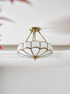 Seen at a close angle against crown moulding, this Clérachic ceiling light's brass frame and glass dome glow warm.