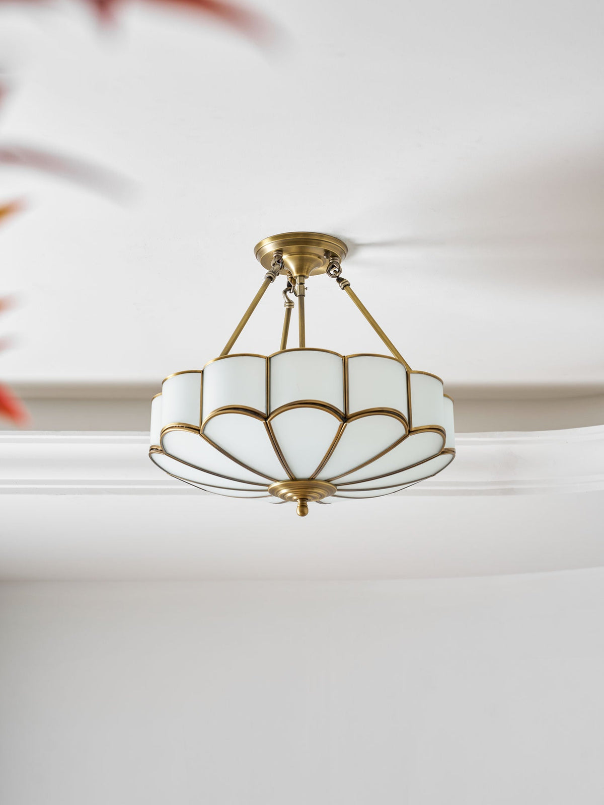 Seen at a close angle against crown moulding, this Clérachic ceiling light's brass frame and glass dome glow warm.
