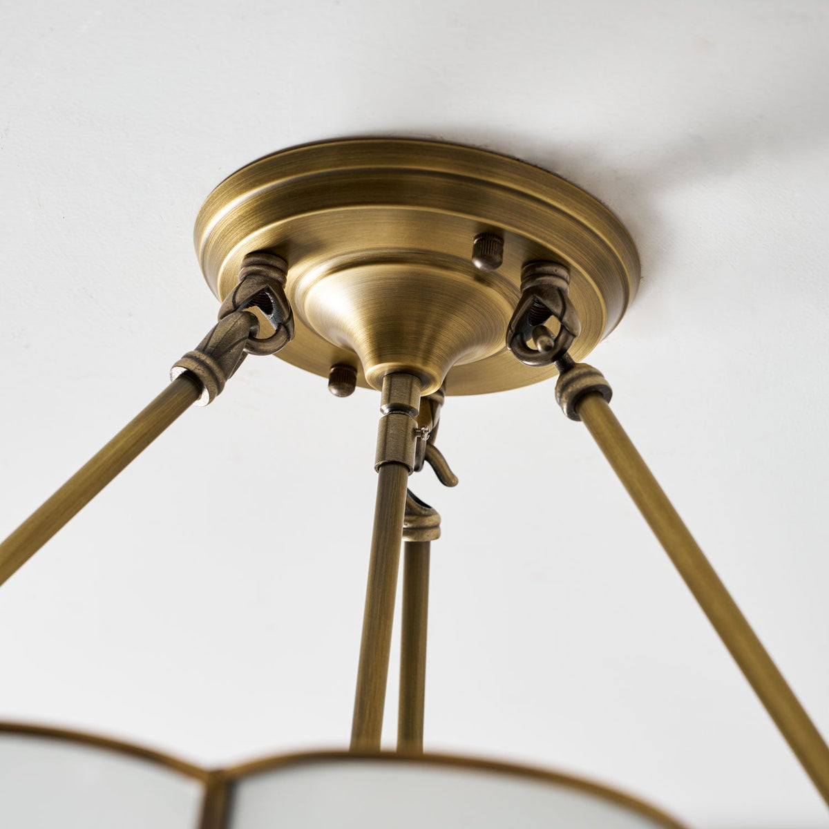 Close view of the brass ceiling canopy and its three support rods on this Clérachic ceiling light, mounted flush to a plain ceiling.