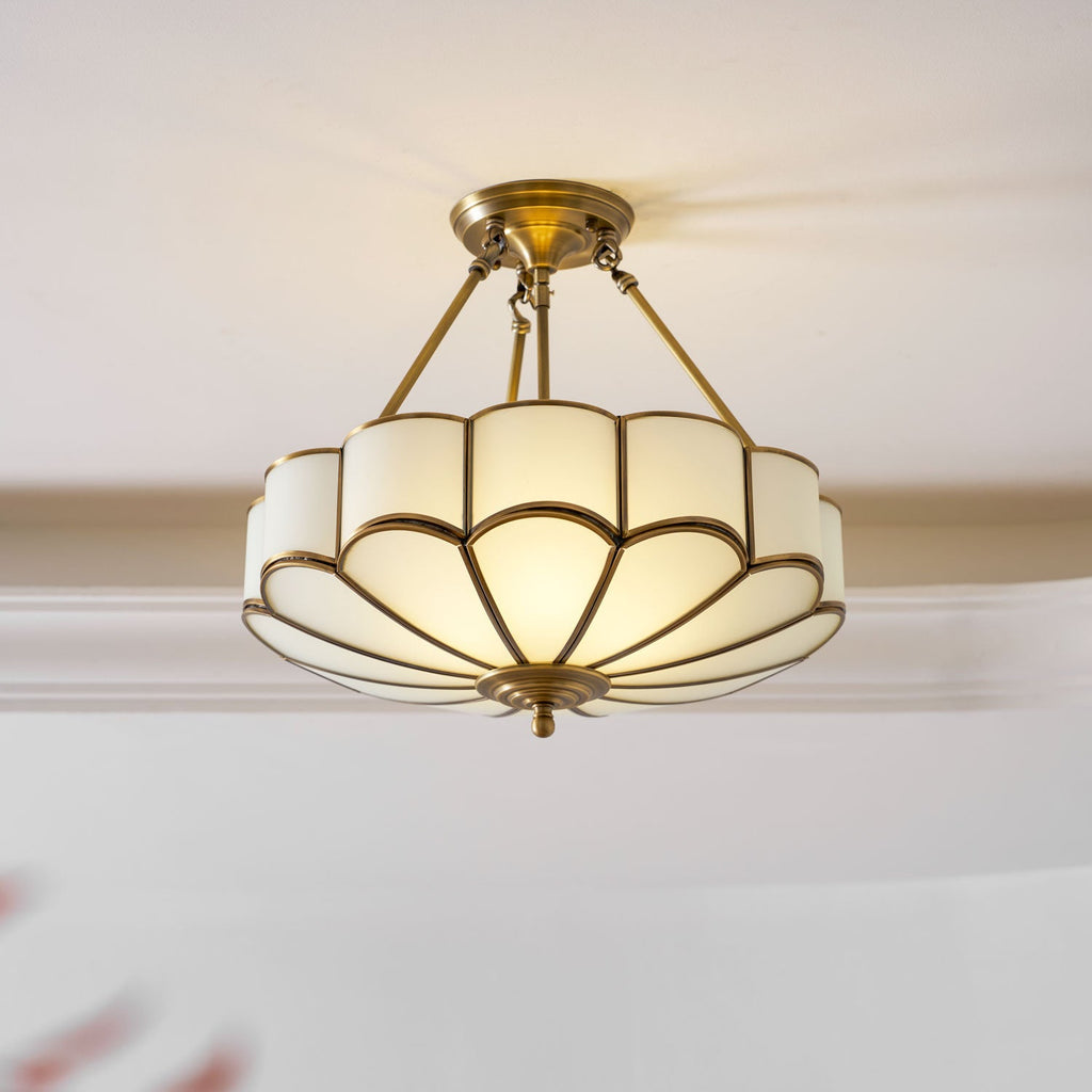 This Clérachic ceiling light hangs close to a crown-moulded ceiling, its scalloped frosted-glass dome glowing warm within a brass frame.