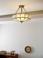 In a plain room with a small wall clock and a low console, this Clérachic ceiling light glows warm near the ceiling.
