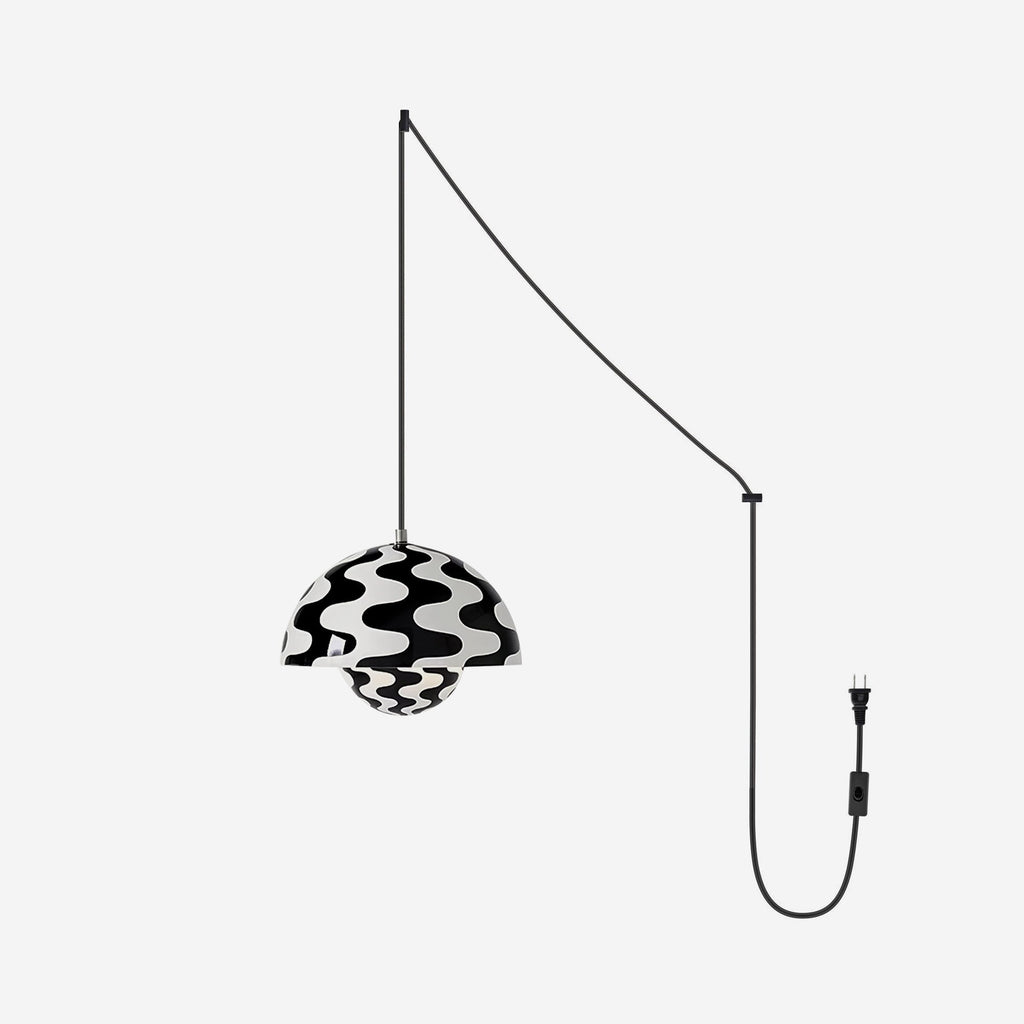 Monochrome wave-print pendant lit on a pale grey backdrop, cord swagged to a plug and switch