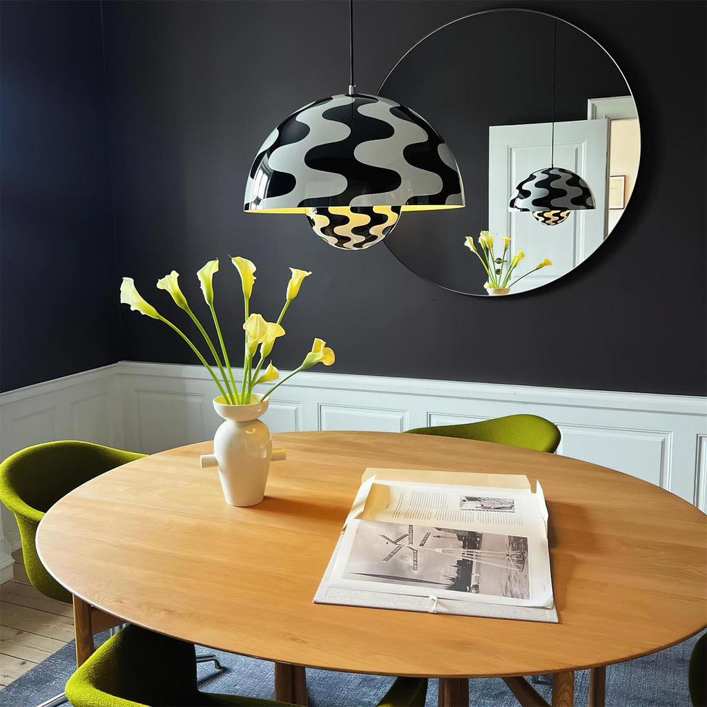The wave-print pendant lit above a round oak dining table against a dark navy dining room wall