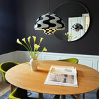 The wave-print pendant lit above a round oak dining table against a dark navy dining room wall