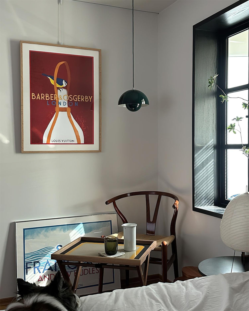 Dark green pendant hanging in a sunlit corner beside a framed print, over a small tray table