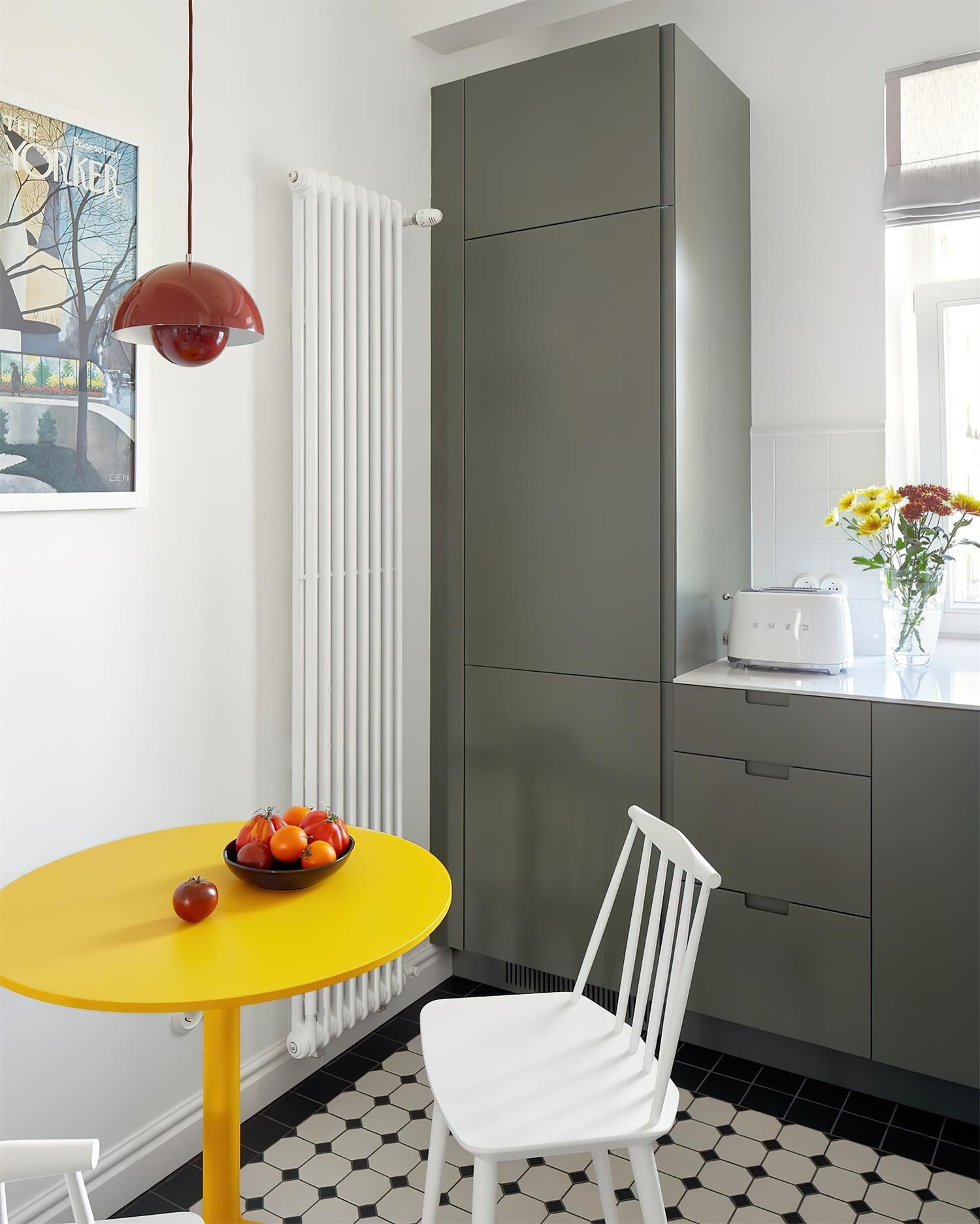 Oxblood red pendant on a red cord above a yellow oval kitchen table set with a bowl of tomatoes