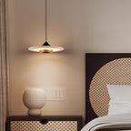Clérachic disc pendant light hangs above a rattan-fronted nightstand holding a round white ceramic vase.