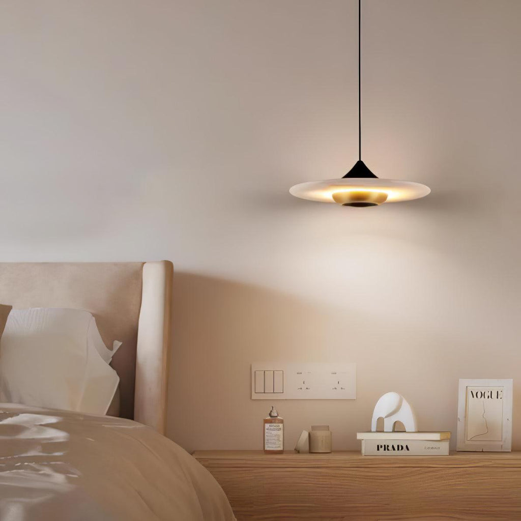 Clérachic flat disc pendant light hangs over a wooden nightstand styled with books, a bottle and a small ornament.