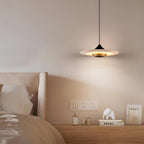 Clérachic flat disc pendant light hangs over a wooden nightstand styled with books, a bottle and a small ornament.