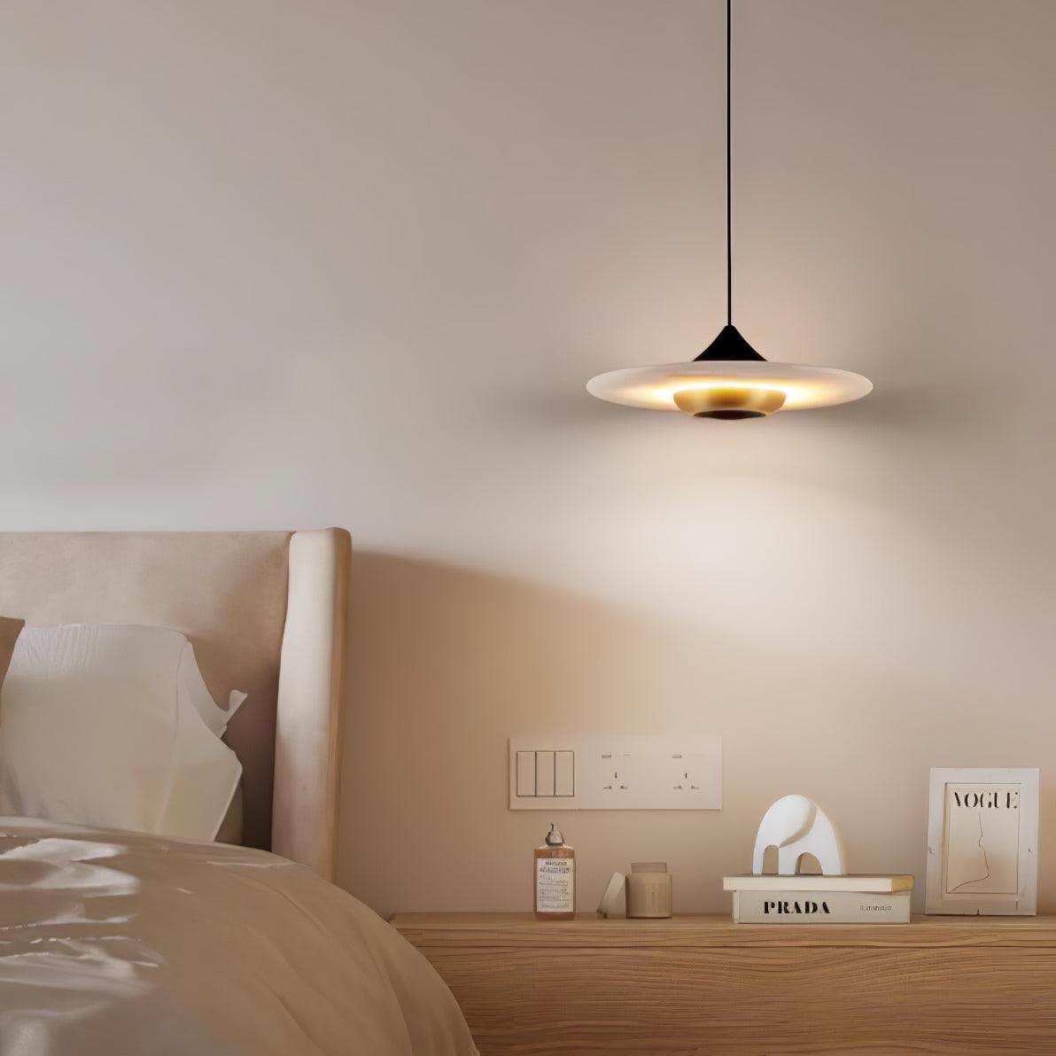 Clérachic flat disc pendant light hangs over a wooden nightstand styled with books, a bottle and a small ornament.