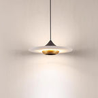 Clérachic white marble disc pendant light glows on its black cord, shown alone against a plain wall.