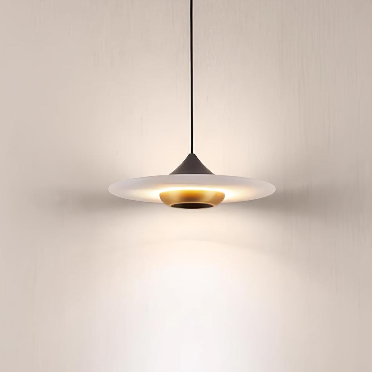 Clérachic white marble disc pendant light glows on its black cord, shown alone against a plain wall.