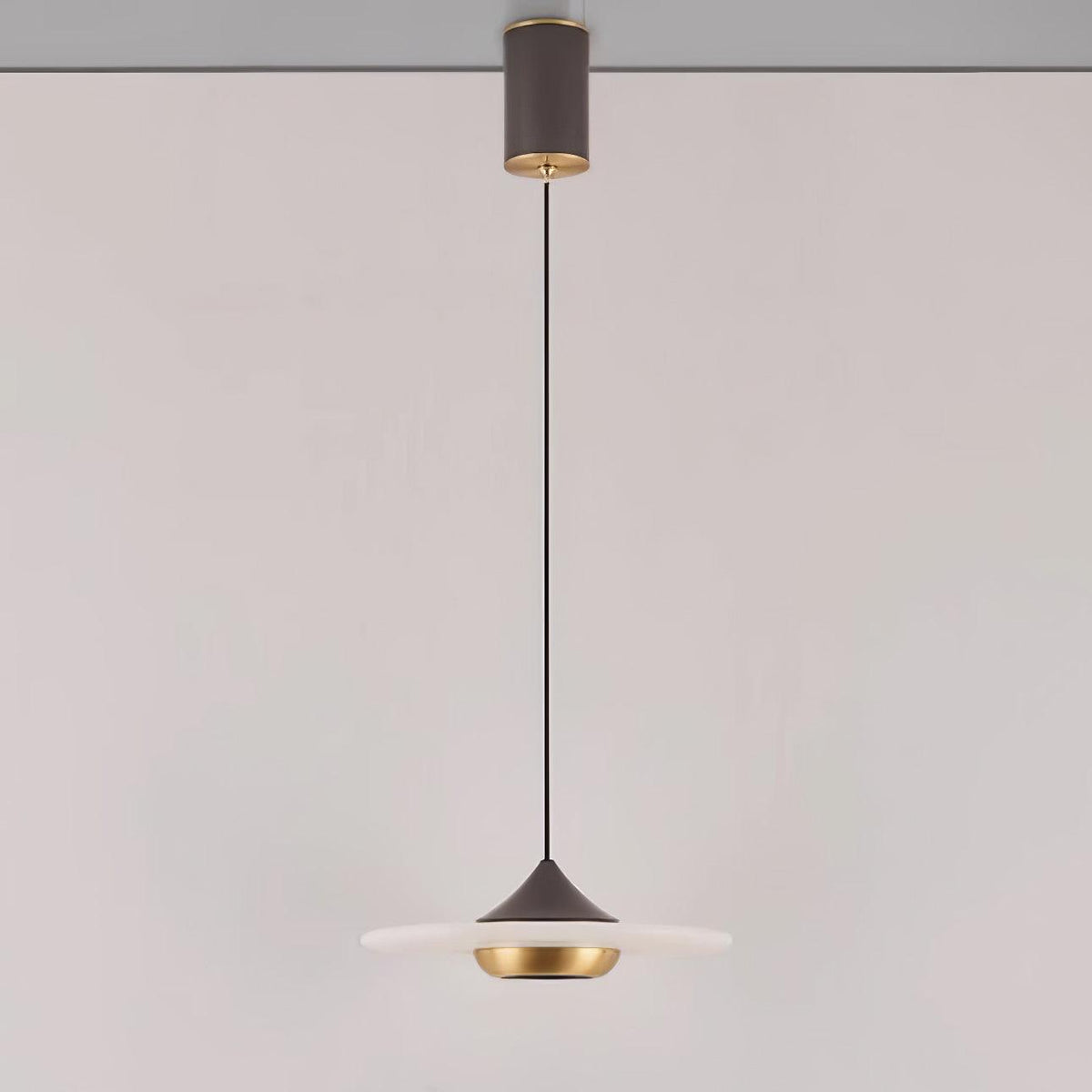 Clérachic flat disc pendant light hangs on a long black cord from its ceiling mount against a plain wall.