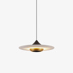 Clérachic pendant light with a wide flat disc shade lit warm underneath, its slim black cord meeting a dark cone fitting and brass ring, shown on white.