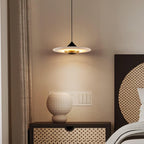 Clérachic flat disc pendant light hangs over a rattan-fronted nightstand holding a textured white vessel.