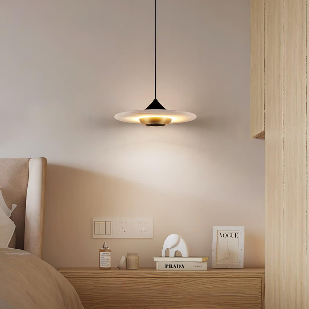 Clérachic white marble disc pendant light hangs low over a bedside table with a perfume bottle and stacked books.