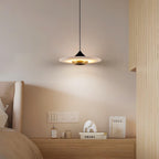 Clérachic white marble disc pendant light hangs low over a bedside table with a perfume bottle and stacked books.
