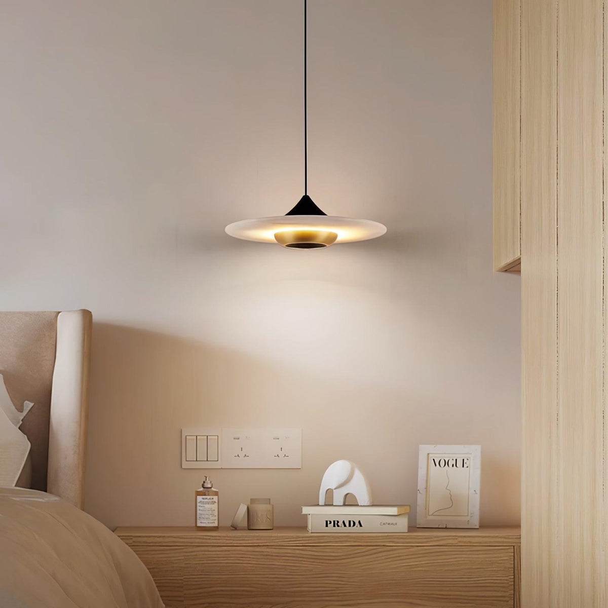 Clérachic white marble disc pendant light hangs low over a bedside table with a perfume bottle and stacked books.
