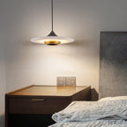 Clérachic disc pendant light hangs above a dark wood nightstand beside a grey upholstered headboard.