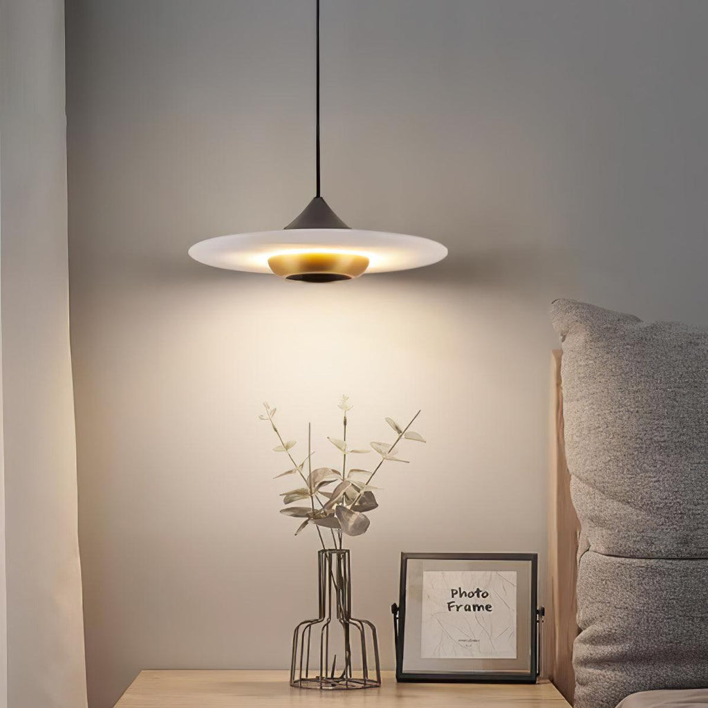 Clérachic flat disc pendant light hangs over a nightstand with a wire vase of eucalyptus and a small picture frame.