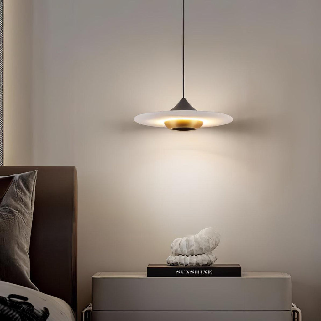 Clérachic disc pendant light glows over a grey nightstand with a small white sculpture and a stack of books.