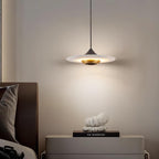 Clérachic disc pendant light glows over a grey nightstand with a small white sculpture and a stack of books.