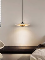 Clérachic flat disc pendant light hangs low over a dark wood bench, cropped close against a plain wall.