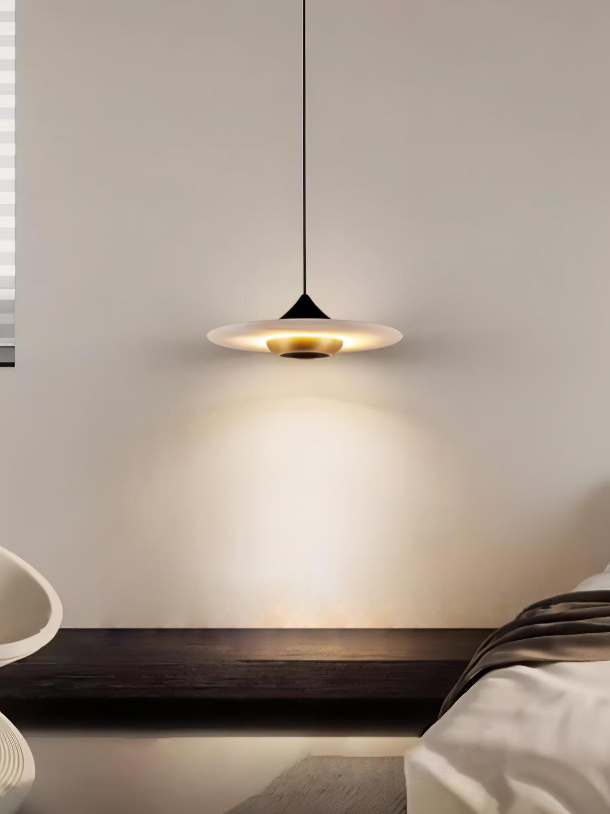 Clérachic flat disc pendant light hangs low over a dark wood bench, cropped close against a plain wall.