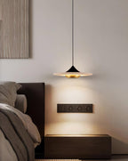 Clérachic disc pendant light hangs above a dark nightstand fitted with twin wall sockets beside the bed.