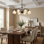 Under a coffered ceiling, the black-finish chandelier from Clérachic hangs above a wood dining table set with white place settings.
