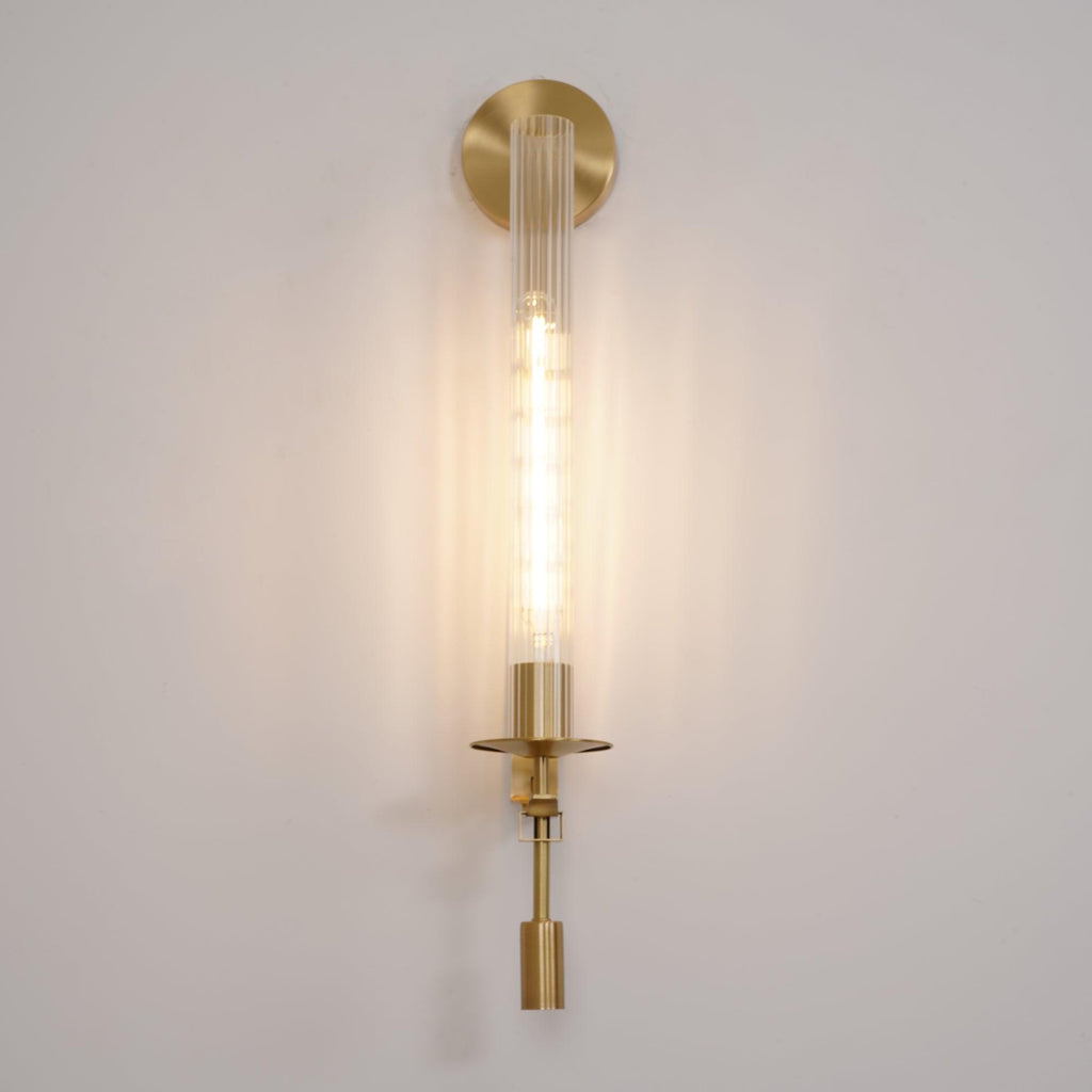 Brass wall lamp with ribbed glass cylinder glowing softly