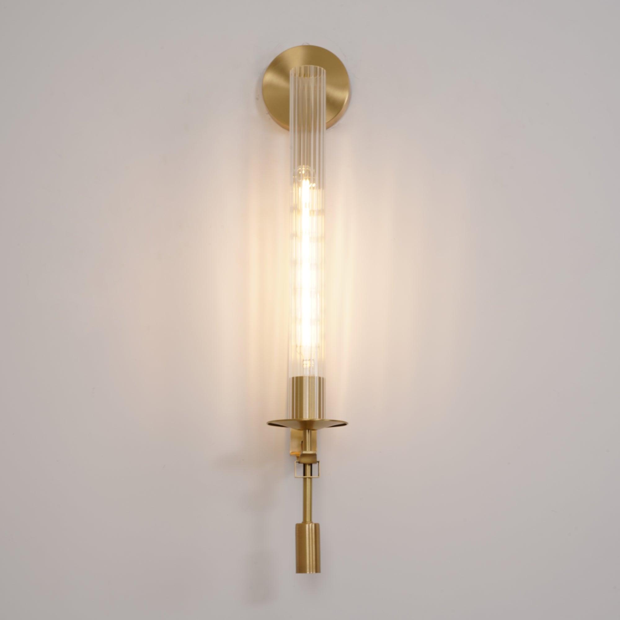 Brass wall lamp with ribbed glass cylinder glowing softly