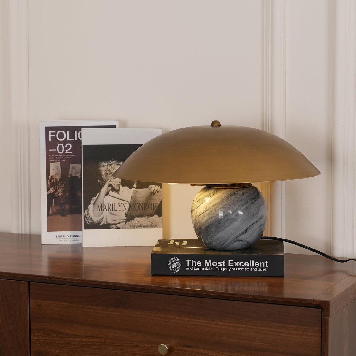 Clérachic lamp lit on a walnut sideboard among framed book covers, its marbled sphere base glowing beneath the shade.