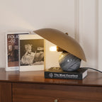 Clérachic lamp lit beside framed book covers on a walnut sideboard, its tilted shade angled toward the light.