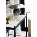 Clérachic lamp on a bar cart shelf beside a decanter and glasses, its tilted bronze shade catching the light.