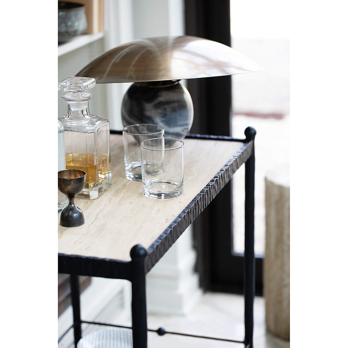 Clérachic lamp on a bar cart shelf beside a decanter and glasses, its tilted bronze shade catching the light.