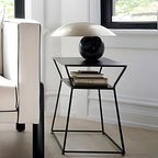 Clérachic lamp in a pewter-toned dome shade on a dark sphere base, shown on an angular black side table in a bright room.
