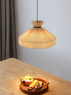 This Clérachic pendant hangs above a wood table corner set with a small bowl of fruit, against a plain grey wall.