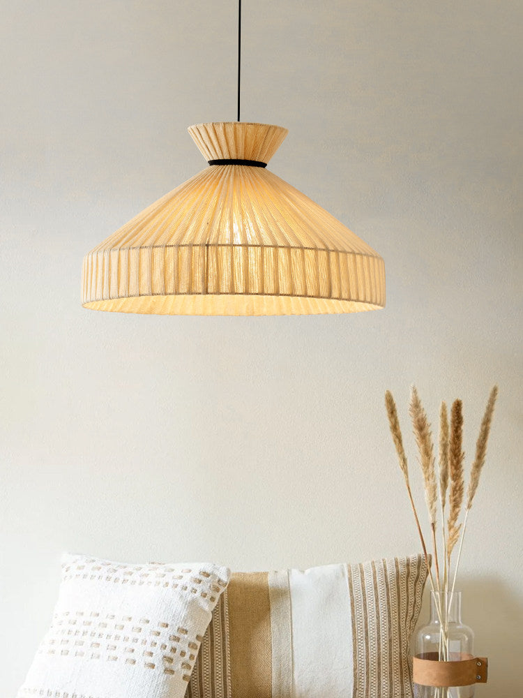 This Clérachic pendant hangs against a plain wall above a striped cushion and a vase of dried pampas grass.