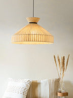 This Clérachic pendant hangs against a plain wall above a striped cushion and a vase of dried pampas grass.