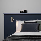 Above a navy headboard with small candles on a shelf, this Clérachic reading light in nickel sits mounted on the wall.