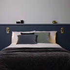 A pair of this Clérachic reading light in bronze flank a navy headboard with pillows, both unlit.