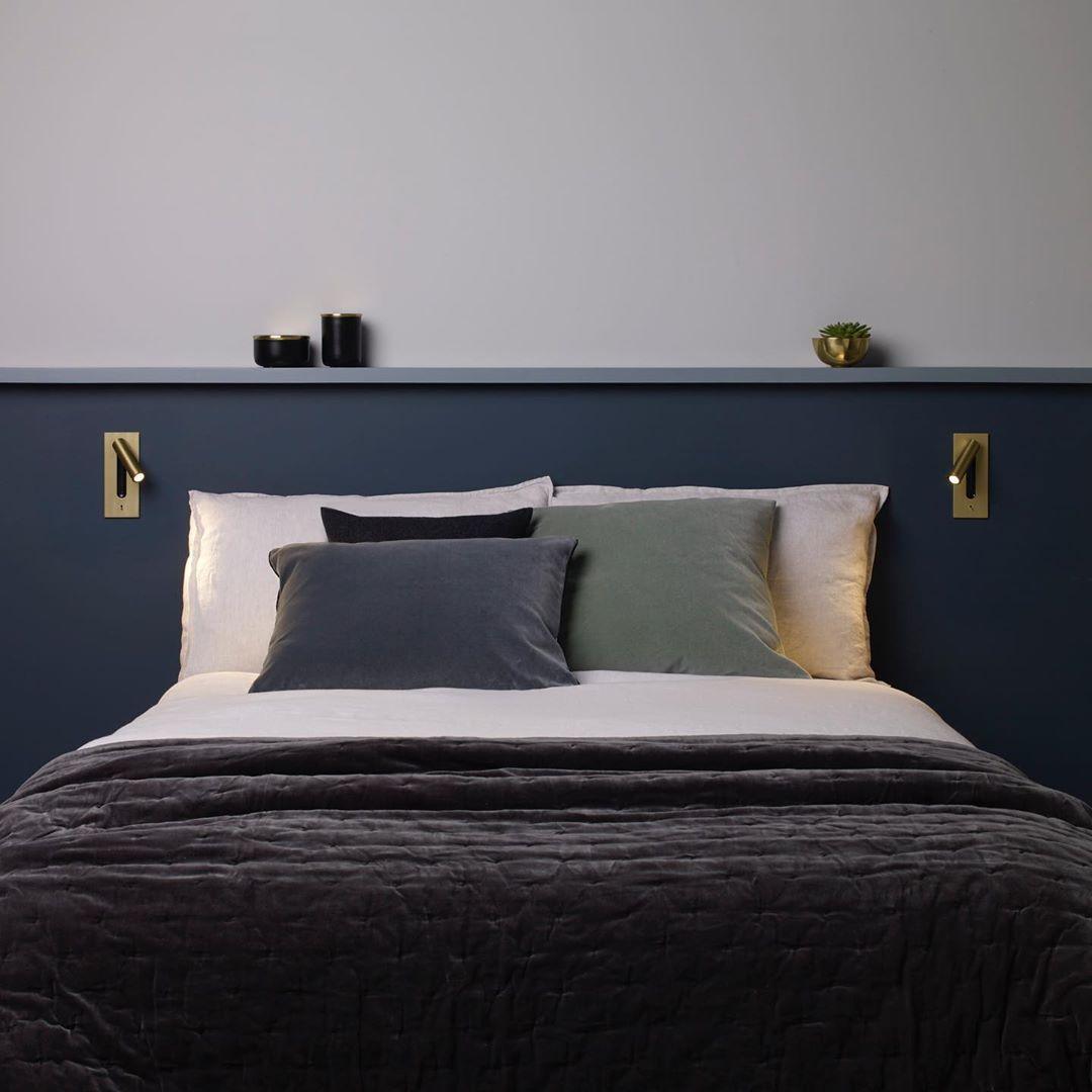 A pair of this Clérachic reading light in bronze flank a navy headboard with pillows, both unlit.