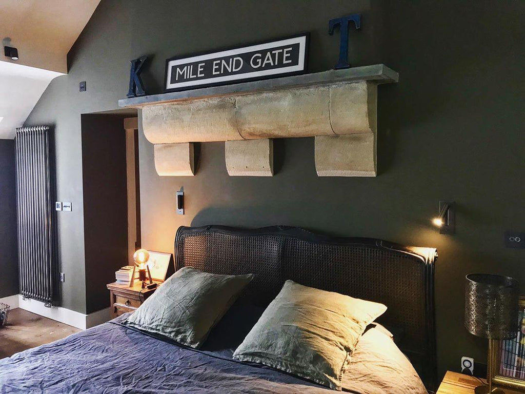 Mounted on a dark green wall above a bed, this Clérachic reading light in nickel sits below a shelf with a decorative sign.