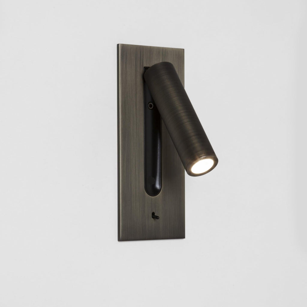 This Clérachic reading light in bronze, lit, swings its head out from a plain white wall mount.