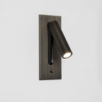 This Clérachic reading light in bronze, lit, swings its head out from a plain white wall mount.