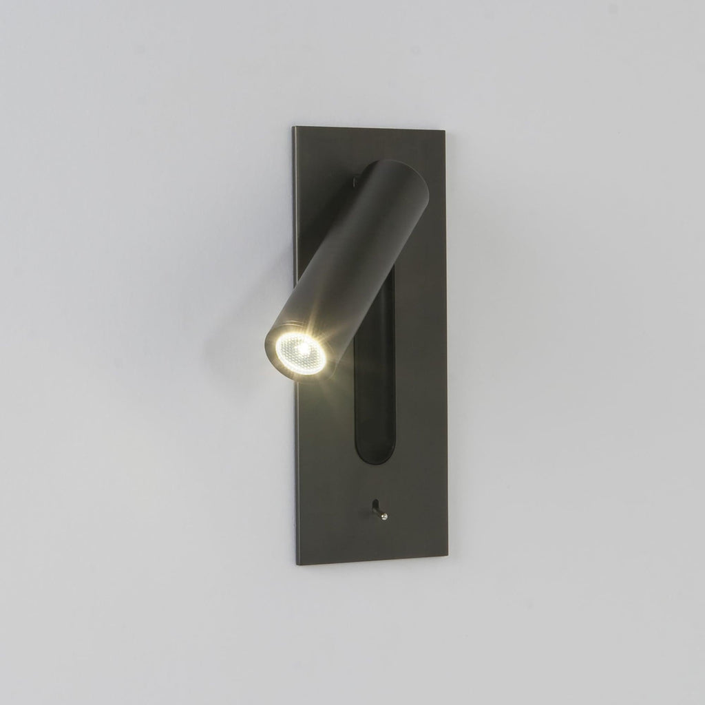 Mounted on a plain grey wall, this Clérachic reading light in bronze glows down at an angle.
