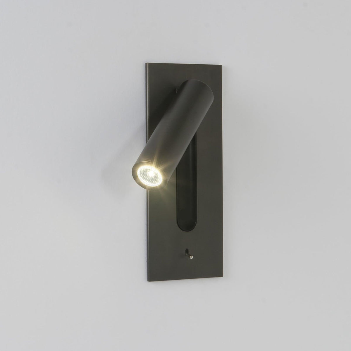 Mounted on a plain grey wall, this Clérachic reading light in bronze glows down at an angle.
