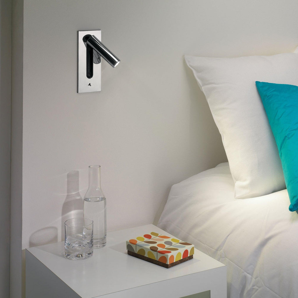 This Clérachic reading light in nickel is mounted above a nightstand with water bottles, beside a teal cushion.