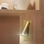 Lit and angled downward, this Clérachic reading light in copper is mounted in a wood-panelled bedroom nook above a shelf.